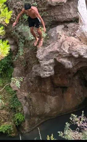 Un chico saltando desde una roca a una poza natural