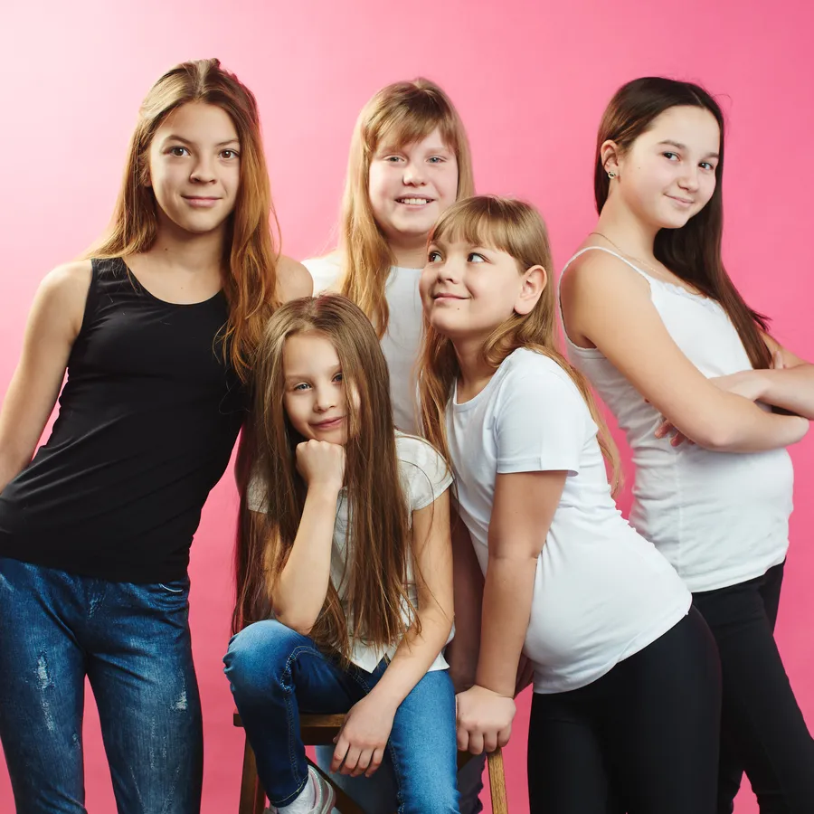 Cinco chicas de entre diez y catorce años posan juntas sobre un fondo rosa
